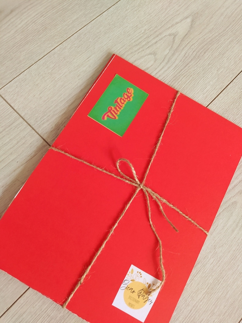 Op de afbeelding: Een rood pakketje gebonden met touw en versierd met twee stickers. E&eacute;n sticker zegt "Vintage" in een retro-lettertype en de andere zegt "Dear Paper" met een bloemenmotief.