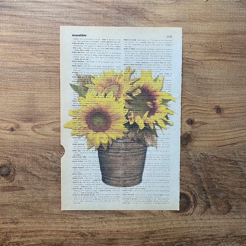 May include: A dictionary page with the word "mandible" highlighted. Two sunflowers are in a pot, with the stems and leaves extending over the page. The sunflowers are yellow with dark brown centers.