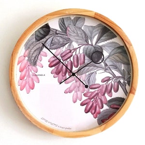 May include: Round wooden wall clock featuring a botanical print of pink and purple berries and gray leaves. The clock face has black hands and the text "CLOUDGNOLA" and "EPHEMERETTE à larges feuilles".