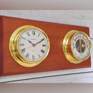 May include: A rectangular mahogany wood plaque featuring a brass-rimmed quartz clock with Roman numerals on the left and a brass-rimmed barometer with a white dial and red and black text on the right. Both instruments are mounted horizontally.