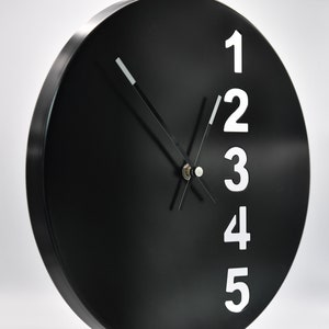 Puede incluir: Un reloj redondo negro con números blancos del 1 al 5 en el lado derecho de la esfera. Las manecillas del reloj son negras.