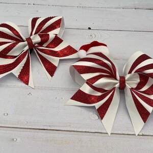 May include: Two red and white striped glitter cheer bows with a Santa hat on one bow.