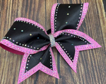 May include: Black cheerleading bow with pink trim and sparkling rhinestones. The bow features a center rhinestone accent and is made of a satin-like material. The bow is designed for cheerleading or dance.