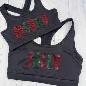 May include: Two black sports bras with the words "merry" and "jolly" spelled out in red and green rhinestones.
