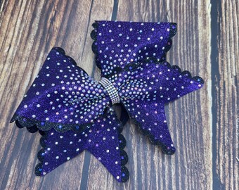 Puede incluir: Un lazo grande para el cabello morado con un acabado brillante y lunares blancos. El lazo tiene un ribete de encaje negro festoneado y un centro de diamantes de imitación. Este accesorio es adecuado para animadoras o baile.