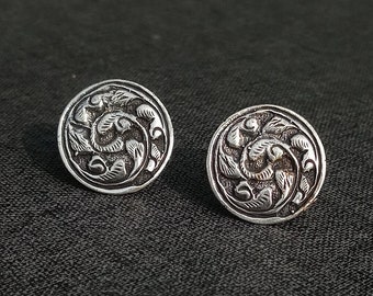 May include: A pair of silver earrings with a circular design featuring intricate floral patterns.
