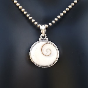 Könnte beinhalten: Eine silberne Kettenkette mit einem runden Anhänger, der eine weiße Muschel mit einem braunen Spiralmuster zeigt.