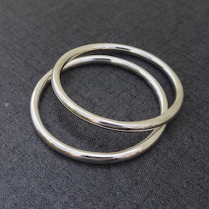 Puede incluir: Dos pulseras de plata, una ligeramente más grande que la otra, están apiladas una encima de la otra. Las pulseras son lisas y brillantes.