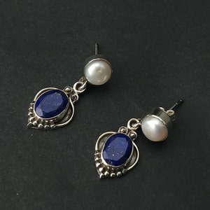 Pode incluir: Um par de brincos de prata com uma pedra preciosa azul e uma p&eacute;rola branca. Os brincos t&ecirc;m um design delicado e ornamentado.