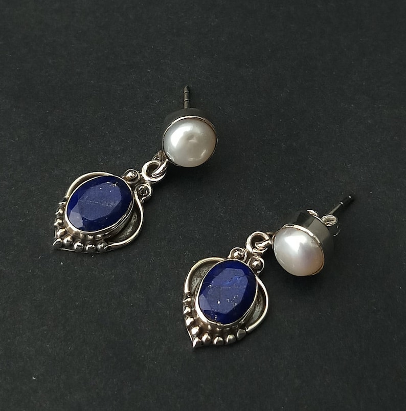 Pode incluir: Um par de brincos de prata com uma pedra preciosa azul e uma p&eacute;rola branca. Os brincos t&ecirc;m um design delicado e ornamentado.