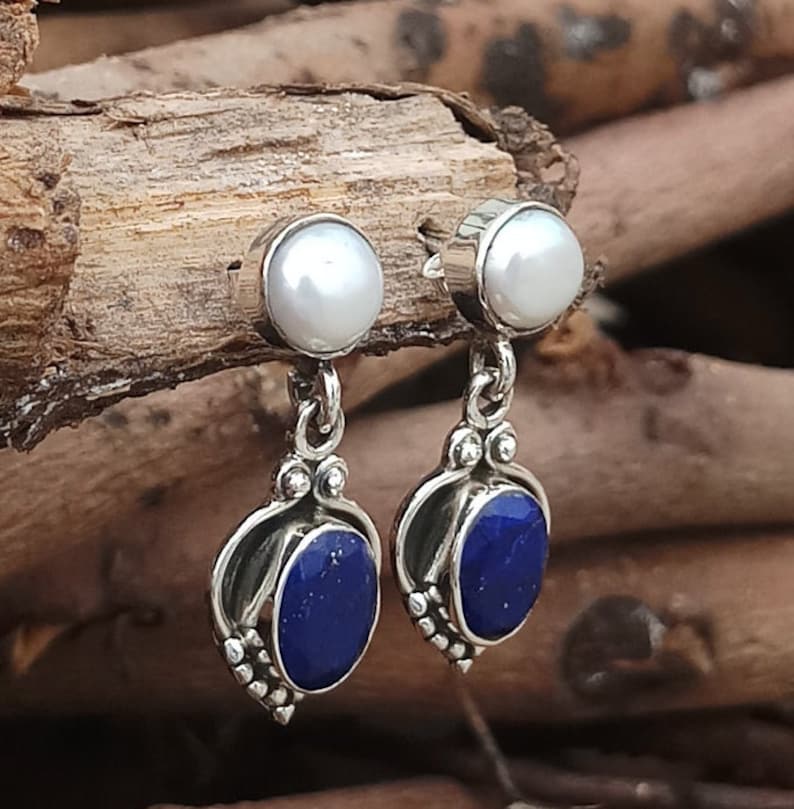 Pode incluir: Brincos de prata esterlina com uma p&eacute;rola branca e uma pedra de l&aacute;pis-laz&uacute;li azul.