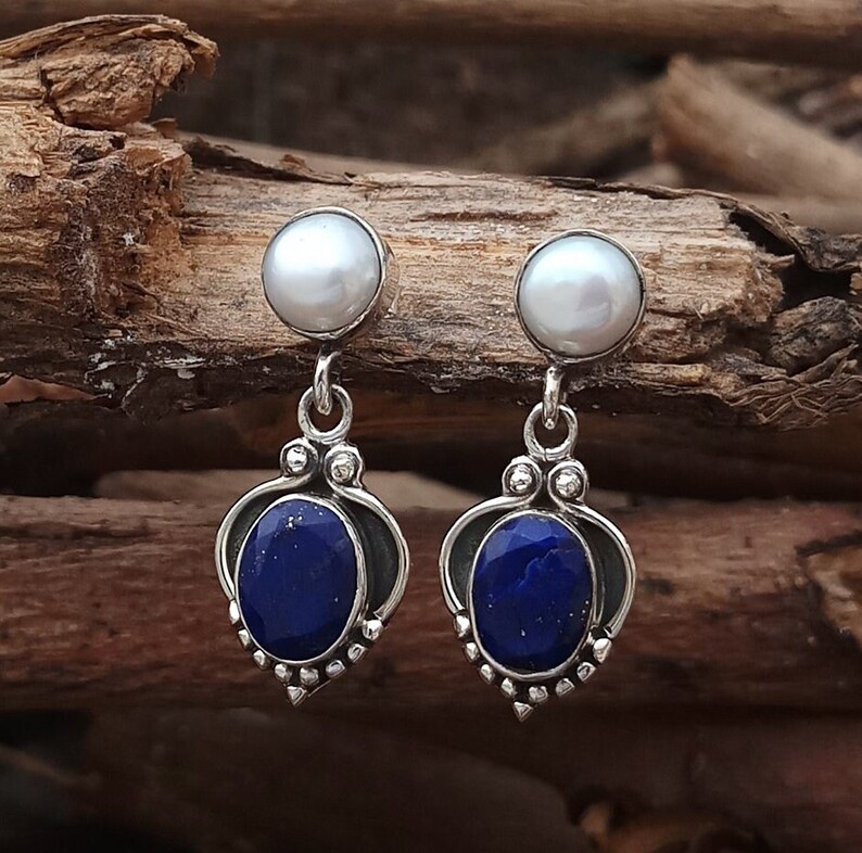 Pode incluir: Um par de brincos de prata com uma pedra de lapis-laz&uacute;li azul e uma p&eacute;rola branca no topo.