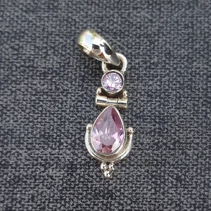 May include: A silver pendant with a teardrop-shaped pink gemstone and a smaller round pink gemstone. The pendant has a decorative design with small beads.
