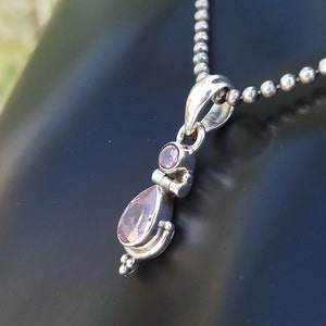 May include: A silver pendant necklace with a teardrop-shaped pink gemstone and a smaller round pink gemstone. The necklace is on a silver chain.