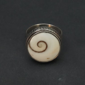 Op de afbeelding: Een zilveren ring met een witte schelp inlay met een bruin spiraalvormig ontwerp.