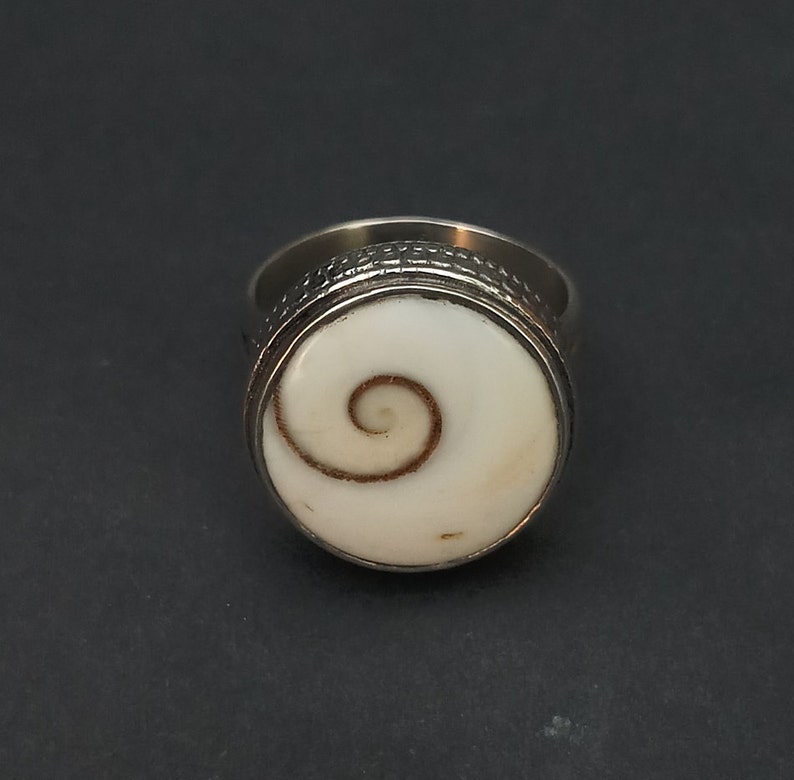 Op de afbeelding: Een zilveren ring met een witte schelp inlay met een bruin spiraalvormig ontwerp.