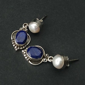 Pode incluir: Um par de brincos de prata com detalhes em lapis-laz&uacute;li azul e p&eacute;rola branca. Os brincos t&ecirc;m a forma de uma l&aacute;grima com uma p&eacute;rola menor na parte superior e uma pedra de lapis-laz&uacute;li maior na parte inferior.