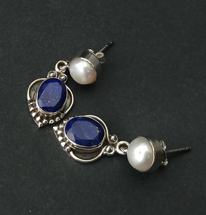 Pode incluir: Um par de brincos de prata com detalhes em lapis-laz&uacute;li azul e p&eacute;rola branca. Os brincos t&ecirc;m a forma de uma l&aacute;grima com uma p&eacute;rola menor na parte superior e uma pedra de lapis-laz&uacute;li maior na parte inferior.
