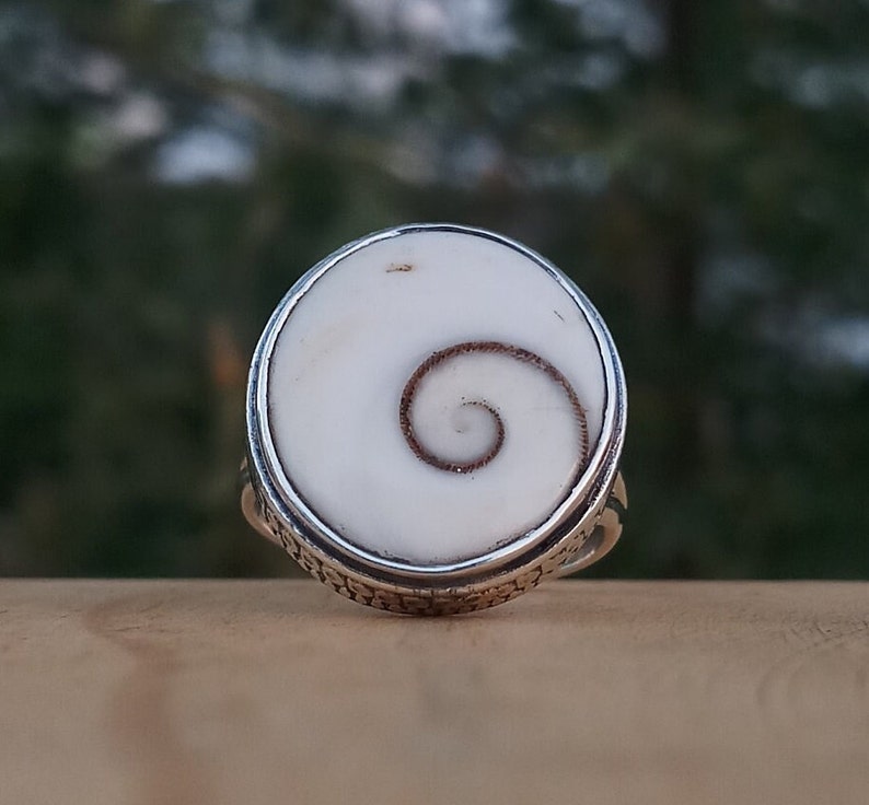 Op de afbeelding: Een zilveren ring met een witte schelp inlay met een bruin spiraalpatroon.