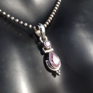 May include: A silver necklace with a pendant featuring a teardrop-shaped purple gemstone and a smaller round purple gemstone.