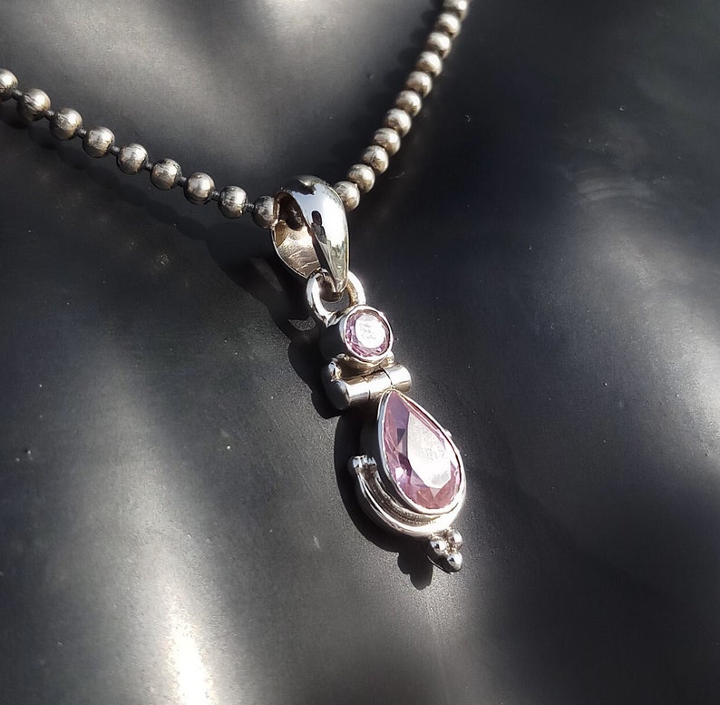 May include: A silver necklace with a pendant featuring a teardrop-shaped purple gemstone and a smaller round purple gemstone.