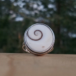 Op de afbeelding: Een zilveren ring met een witte en bruine schelp inlay met een spiraalvormig ontwerp.