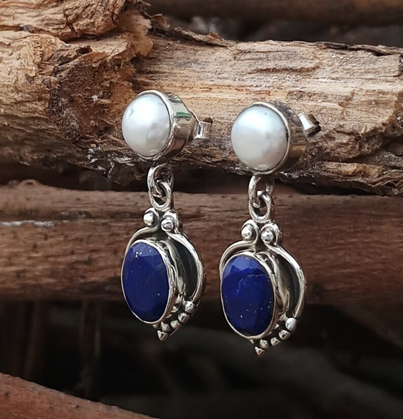 Pode incluir: Um par de brincos de prata com uma p&eacute;rola branca e uma pedra de l&aacute;pis-laz&uacute;li azul. Os brincos t&ecirc;m um design delicado com um pequeno pingente de prata.