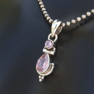 May include: A silver pendant necklace with a teardrop-shaped pink gemstone and a smaller round pink gemstone. The necklace has a silver chain.