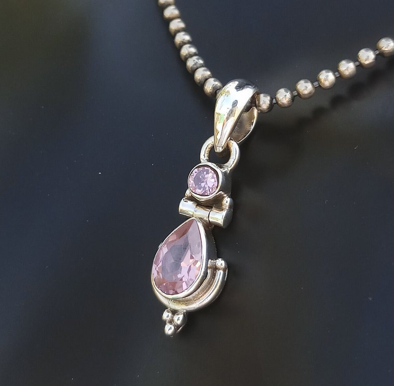 May include: A silver pendant necklace with a teardrop-shaped pink gemstone and a smaller round pink gemstone. The necklace has a silver chain.