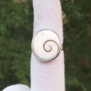 Op de afbeelding: Een zilveren ring met een witte schelp inlay met een bruin spiraalontwerp.
