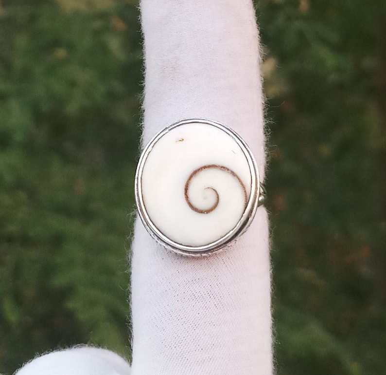 Op de afbeelding: Een zilveren ring met een witte schelp inlay met een bruin spiraalontwerp.