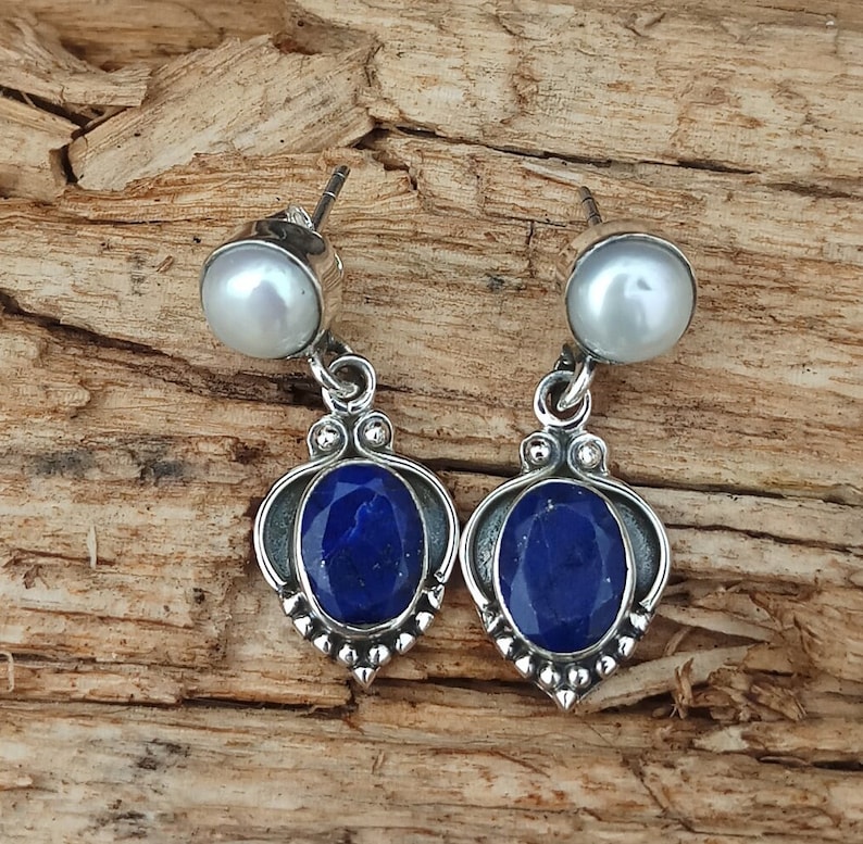 Pode incluir: Um par de brincos de prata com uma pedra de l&aacute;pis-laz&uacute;li azul e uma p&eacute;rola branca. Os brincos t&ecirc;m um design delicado e ornamentado.
