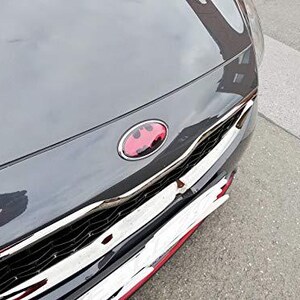 Peut inclure: Gros plan sur le capot gris foncé d'une voiture avec un emblème rouge et argenté. La calandre avant de la voiture est chromée avec des accents rouges. L'image est prise à l'extérieur sur une surface pavée grise.
