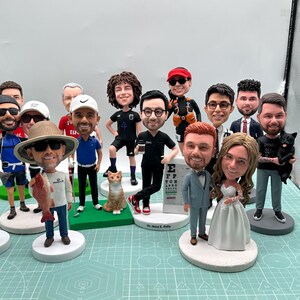 May include: A collection of custom bobblehead figurines, each depicting a person in various outfits and poses. Some hold objects like fish, a cat, and a coffee cup. The figurines are on white circular bases.