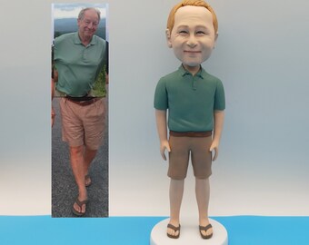 May include: A custom-made figurine of a person wearing a green polo shirt and khaki shorts. The figurine is standing on a white base.