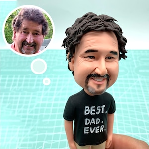 May include: A caricature figurine of a person with brown hair and a beard wearing a black t-shirt with the text "BEST DAD EVER" in white lettering.