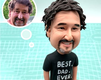 May include: A caricature figurine of a person with brown hair and a beard wearing a black t-shirt with the text "BEST DAD EVER" in white lettering.