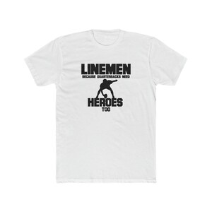 Könnte beinhalten: Weißes T-Shirt mit schwarzem Text, der "Linemen because quarterbacks need heroes too" lautet. Im Zentrum des Textes ist eine Silhouette eines Footballspielers abgebildet.