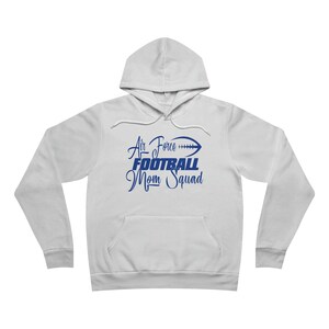 Puede incluir: Una sudadera con capucha blanca con un gráfico azul que dice "Air Force Football Mom Squad" con un gráfico de fútbol.