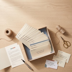 May include: A set of cream-colored envelopes labeled Open When in a box, accompanied by a letter, a pen, a spool of twine, scissors, and small cards with text including Open when you are homesick and Open when you need a laugh.