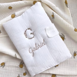 Peut inclure: Tapis à langer pour bébé en mousseline blanche avec une lettre G brodée de fleurs et le nom Gabriel brodé en dessous.