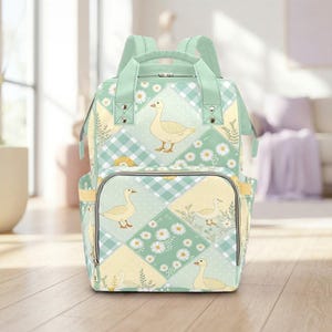 Peut inclure: Un sac à dos patchwork vert menthe et jaune avec un motif fantaisiste d'oie et de marguerites. Le sac à dos comporte plusieurs poches, des bretelles réglables et une poignée supérieure. Le design comprend un mélange de carreaux, de pois et d'éléments floraux.