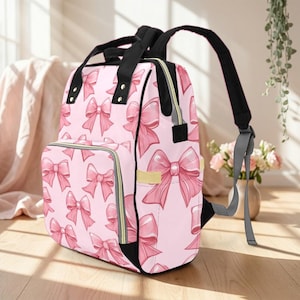 May include: Pink backpack with a repeating pattern of pink bows. The backpack has black straps and a black handle. The zipper is yellow. The backpack has a front pocket and side pocket.