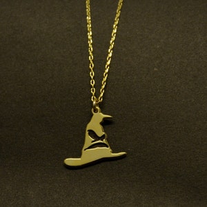 May include: A gold-colored necklace featuring a pendant shaped like a wizard's hat. The hat pendant has a cutout design and hangs from a delicate chain. The necklace is displayed against a dark background.