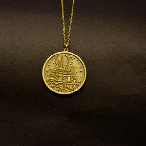 May include: Gold-colored pendant necklace featuring a detailed castle design within a circular frame. The pendant hangs from a delicate chain. The castle design includes turrets, windows, and a full moon, set against a starry sky.