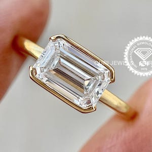 May include: A gold ring with a large, clear emerald-cut diamond. The ring is on a finger and the diamond is sparkling.