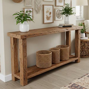May include: A rectangular wooden console table with a rough, natural texture and a lower shelf. The table features four sturdy legs and is positioned against a wall decorated with various woven wall baskets, framed art prints, and a hanging plant.