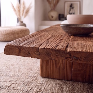 May include: A low coffee table constructed from a thick, solid slab of reclaimed brown wood with a deeply textured, weathered grain. The table features a rectangular top with visible natural cracks and a sturdy, block-style base support.