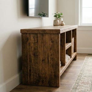May include: A rectangular wooden media console featuring a dark brown finish with visible wood grain texture. The unit includes multiple open storage shelves and a flat top surface, providing a sturdy structure for organizing items in a living space.