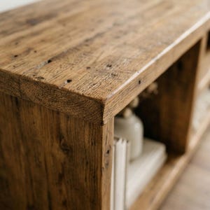 May include: A rectangular wooden media console featuring a weathered brown finish with visible wood grain, knots, and natural imperfections. The unit includes open shelving compartments, with one section containing a white vase and books.